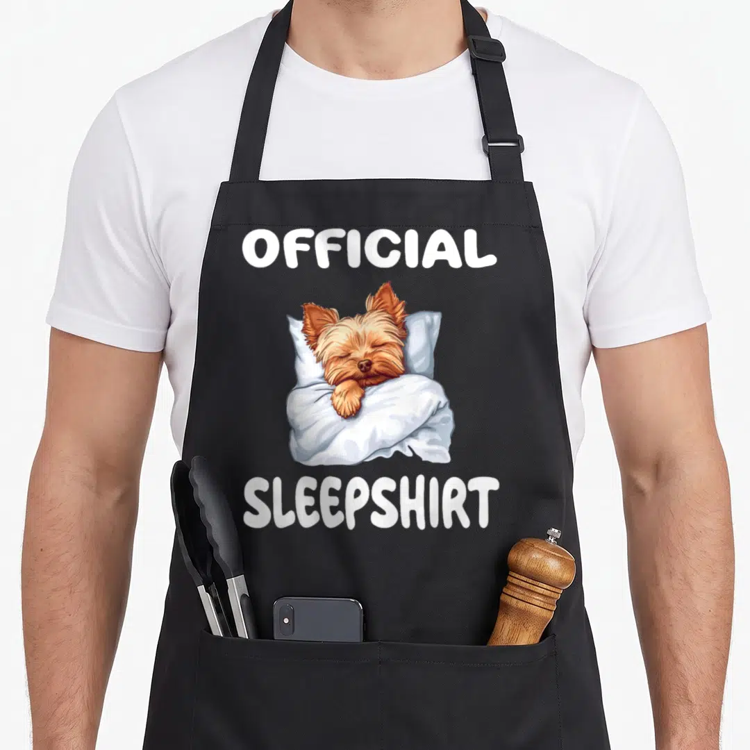 Yorkshire terrier dog apron - Cartoon brown dog sleeping on blue pillow under white blanket with Official Sleepshirt — shown on a black cotton canvas apron against a white background