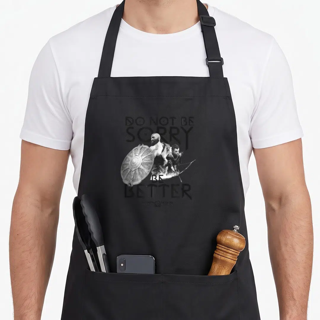 Sorry wars classic apron - Kratos shield Atreus bow DO NOT BE SORRY BE BETTER text God of War logo — shown on a black cotton canvas apron against a white background