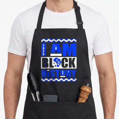 History sorority apron - 1920 I AM BLACK HISTORY text with Africa map silhouette and blue white zigzag borders — shown on a black cotton canvas apron against a white background