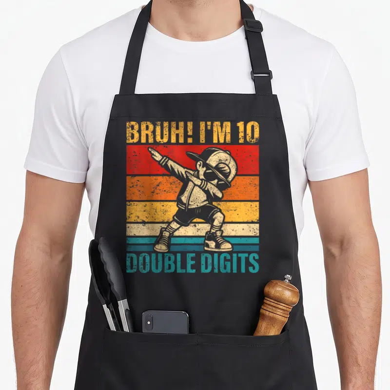 Bruh double digit birthday apron - Dabbing boy over five retro stripes with text BRUH I M 10 DOUBLE DIGITS — shown on a black cotton canvas apron against a white background