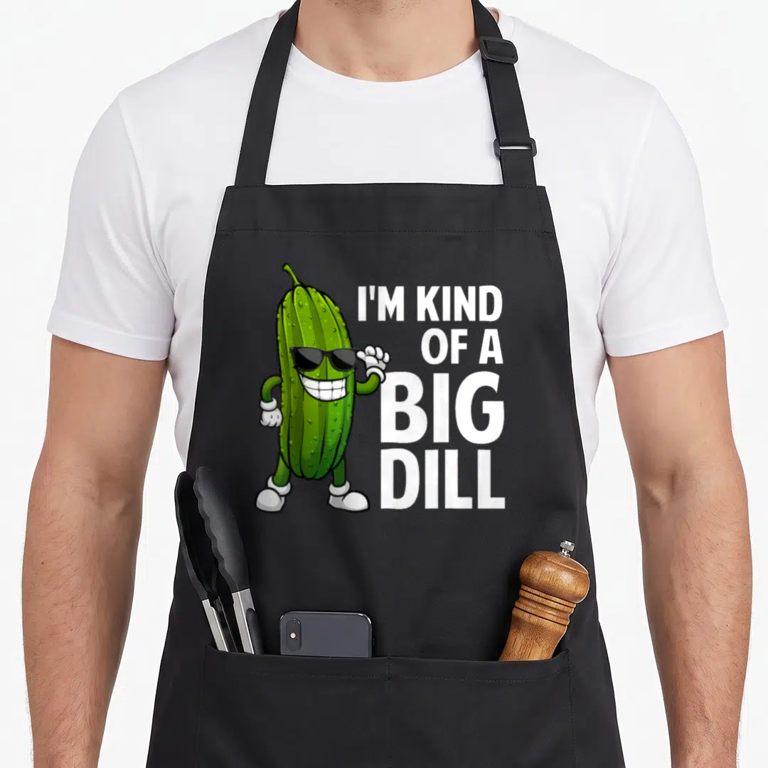Funny dill pickle apron - Cartoon pickle with sunglasses and I'M KIND, OF A, BIG, DILL text in green white black — shown on a black cotton canvas apron against a white background