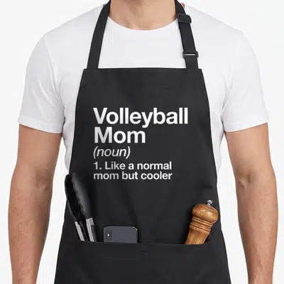 Definition sassy apron - White text reading Volleyball Mom noun like a normal mom but cooler — shown on a black cotton canvas apron against a white background