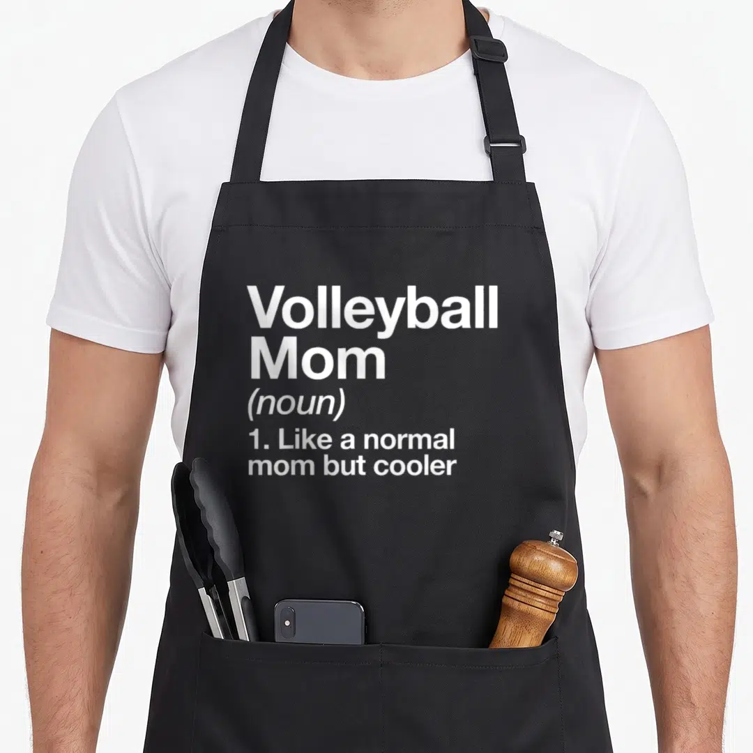 Definition sassy apron - White text reading Volleyball Mom noun like a normal mom but cooler — shown on a black cotton canvas apron against a white background