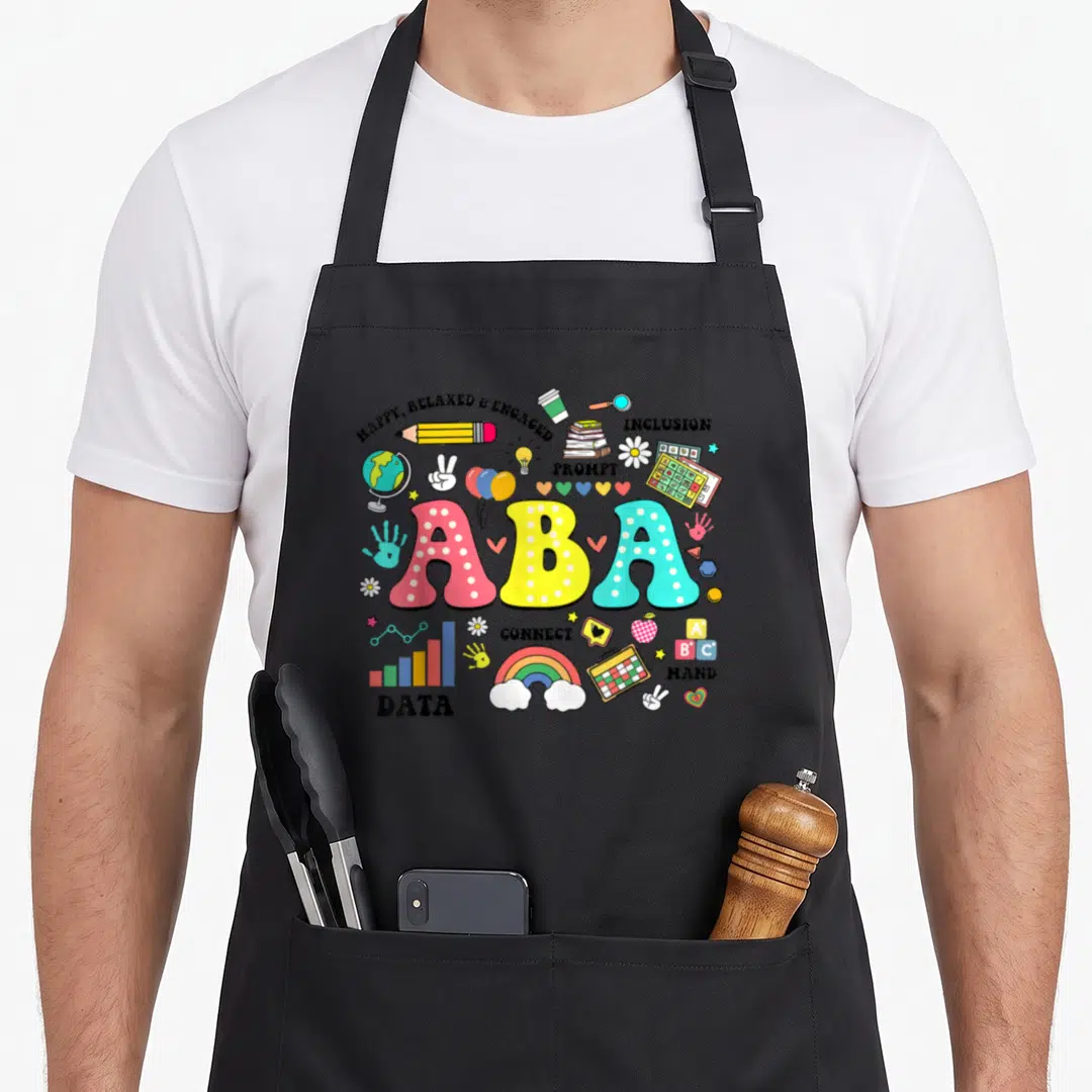Aba floral apron - Cartoon ABA text surrounded by pencil, books, rainbow, and data chart icons in pink yellow blue red — shown on a black cotton canvas apron against a white background