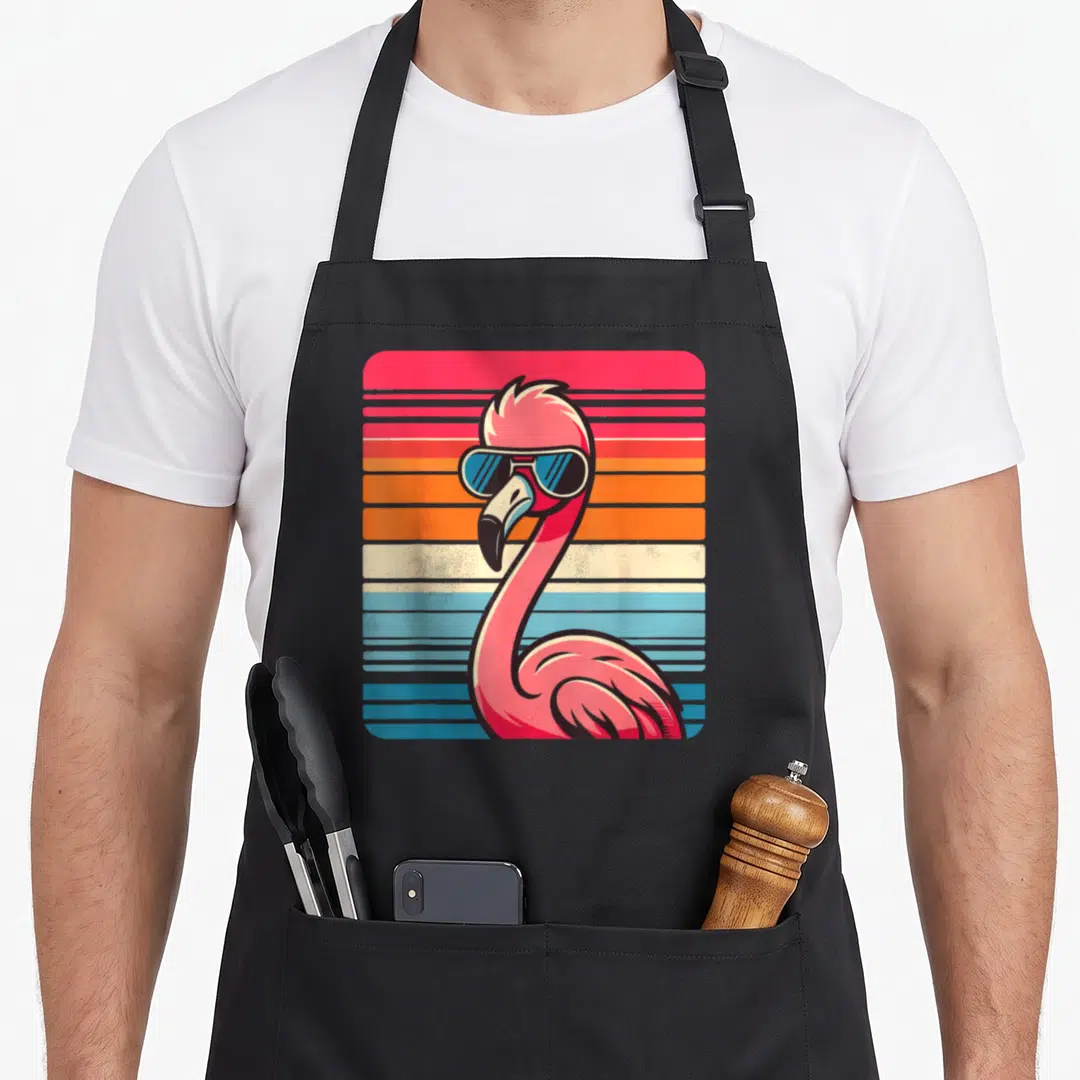 Sunglass flamingo apron - Pink flamingo wearing blue sunglasses against horizontal orange and blue stripes — shown on a black cotton canvas apron against a white background