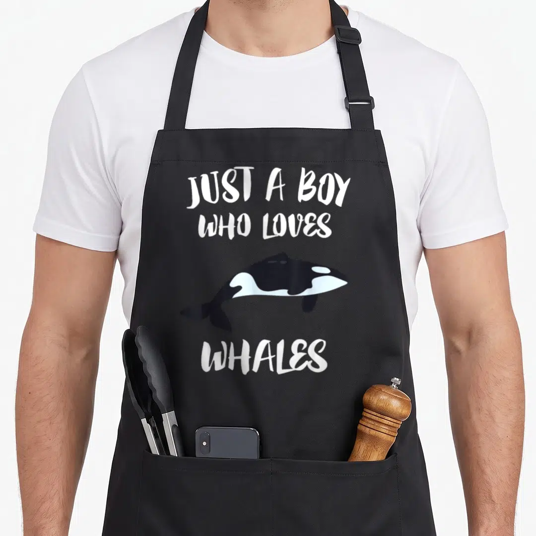 Whale killer orca apron - Cartoon orca between white text JUST A BOY WHO LOVES WHALES — shown on a black cotton canvas apron against a white background
