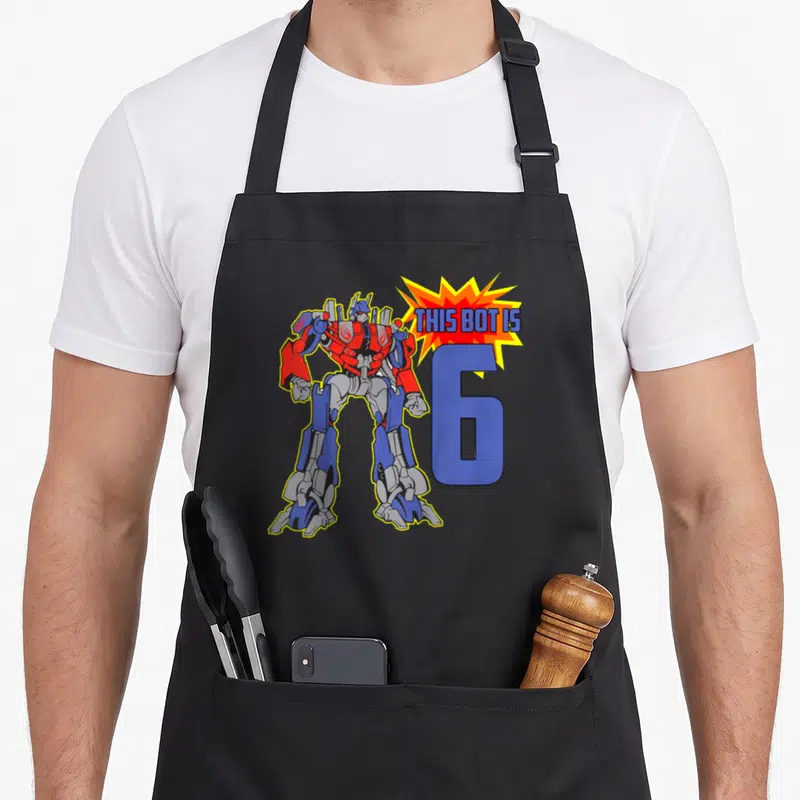 Robot 6th birthday apron - Cartoon robot stands beside large blue number 6 and explosion graphic with text — shown on a black cotton canvas apron against a white background