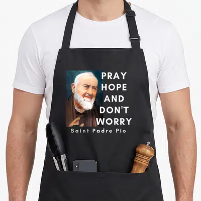 Pio catholic apron - Portrait of Padre Pio with stacked Pray Hope Don't Worry text in white brown and blue — shown on a black cotton canvas apron against a white background