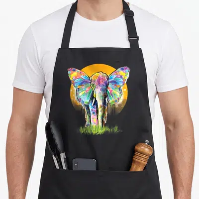 Elephant print apron for men - Multicolored watercolor elephant in front of orange sun with green grass — shown on a black cotton canvas apron against a white background
