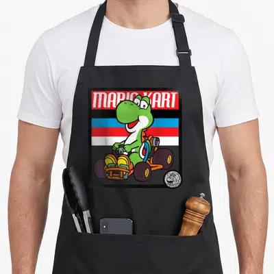 School karting apron - Yoshi driving an orange kart under MARIO KART text with blue red and white stripes — shown on a black cotton canvas apron against a white background