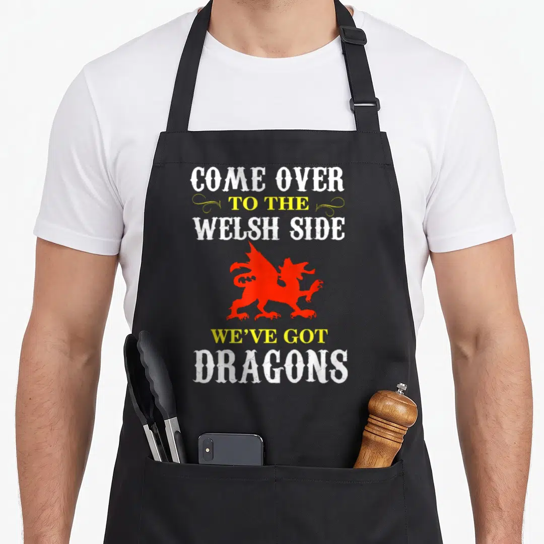 Come welsh apron - Red dragon silhouette between white and yellow text blocks with two swirls — shown on a black cotton canvas apron against a white background