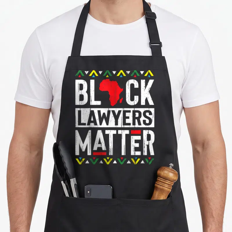 Month lawyer apron - Red Africa map as A in BLACK LAWYERS MATTER, distressed white text, colored triangle borders top — shown on a black cotton canvas apron against a white background