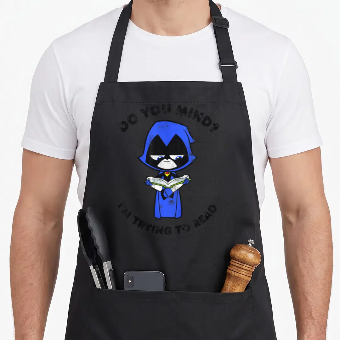 Trying ravens aprons - Cartoon raven in blue cloak holding book with text DO YOU MIND I'M TRYING TO READ — shown on a black cotton canvas apron against a white background