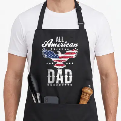 Eagle father day apron - Distressed eagle with American flag wings surrounded by stars and All American Dad text — shown on a black cotton canvas apron against a white background