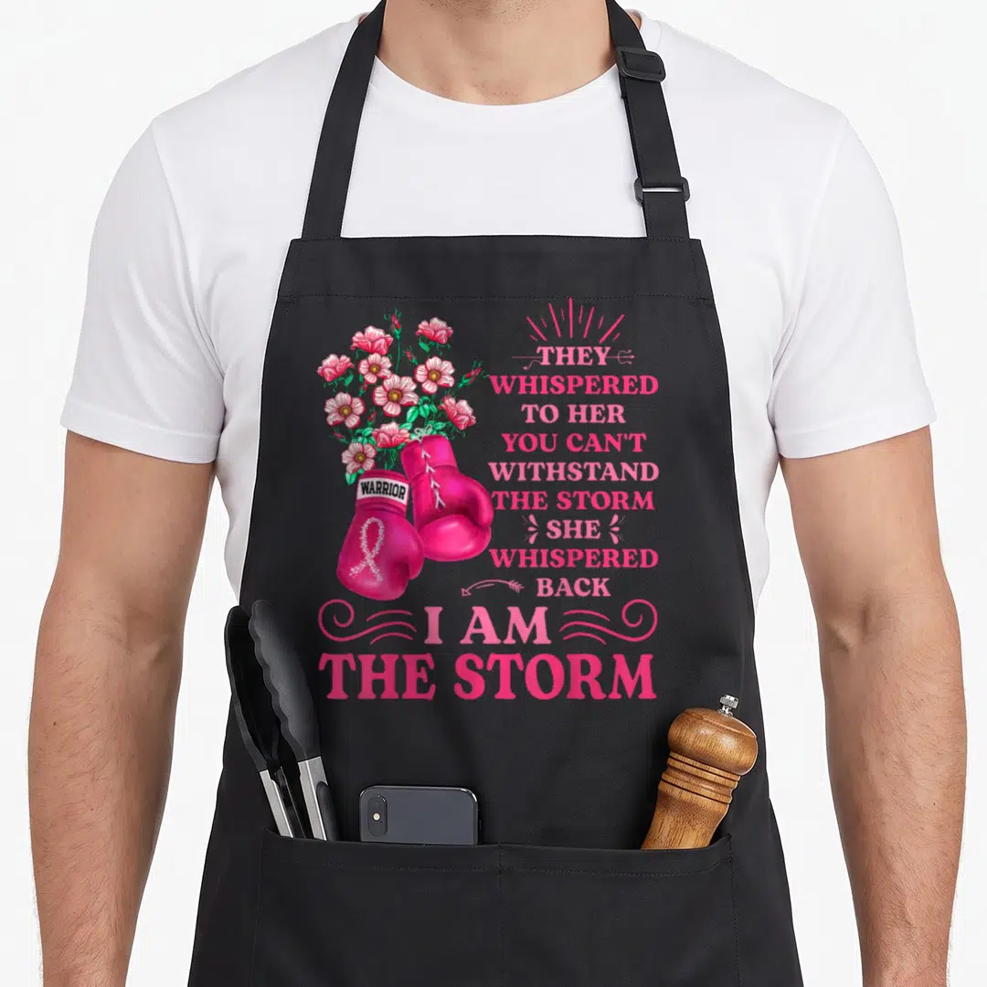 Storm ribbon apron - Pink boxing gloves with white ribbon and bouquet of pink flowers beside stacked inspirational text — shown on a black cotton canvas apron against a white background