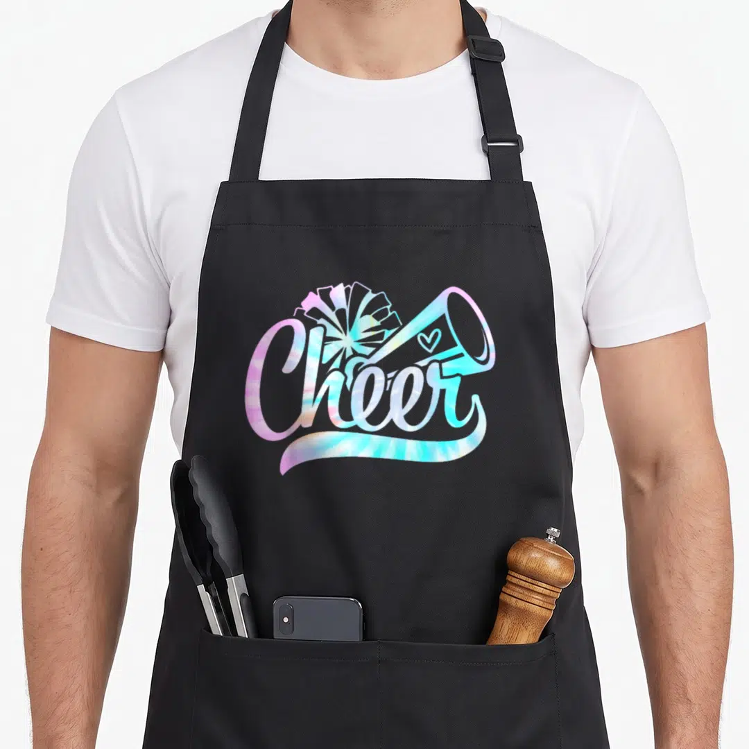 Cheerleading tie-dye apron - Tie-dye Cheer text with pom-pom megaphone heart pink blue yellow — shown on a black cotton canvas apron against a white background