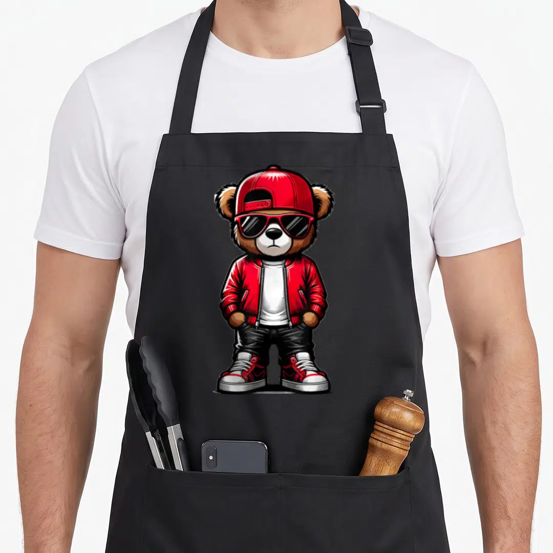 Hop teddy bear apron - Cartoon bear in red cap, sunglasses, red jacket, and black pants standing centrally — shown on a black cotton canvas apron against a white background