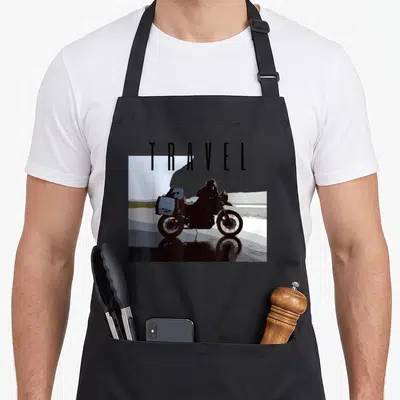 Travel adventure bike apron - Minimalist motorcyclist on touring bike facing right under large TRAVEL text in black — shown on a black cotton canvas apron against a white background