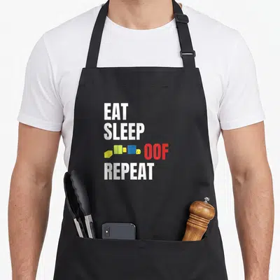 Eat meme apron - Stacked text EAT SLEEP OOF REPEAT with a small blocky character next to the red OOF word — shown on a black cotton canvas apron against a white background