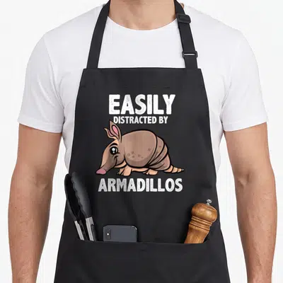 Armadillo lover easily apron - Cartoon brown armadillo with pink nose below white text EASILY DISTRACTED BY ARMADILLOS — shown on a black cotton canvas apron against a white background