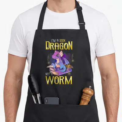 Funny book dragon apron - Purple cartoon dragon on books with text I'M A BOOK DRAGON NOT A WORM — shown on a black cotton canvas apron against a white background