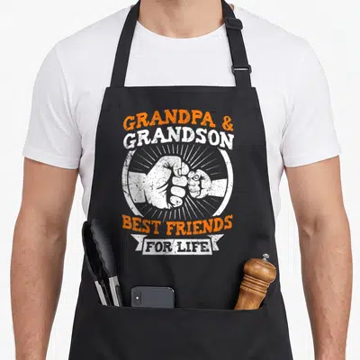 Grandchildren friends apron - Fist bump graphic with Grandpa and Grandson Best Friends For Life text in orange — shown on a black cotton canvas apron against a white background