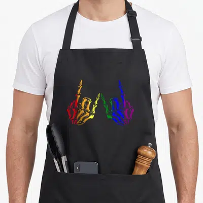Rainbow skeleton apron - Two mirrored skeletal hands colored in red, orange, yellow, green, blue, and purple stripes — shown on a black cotton canvas apron against a white background