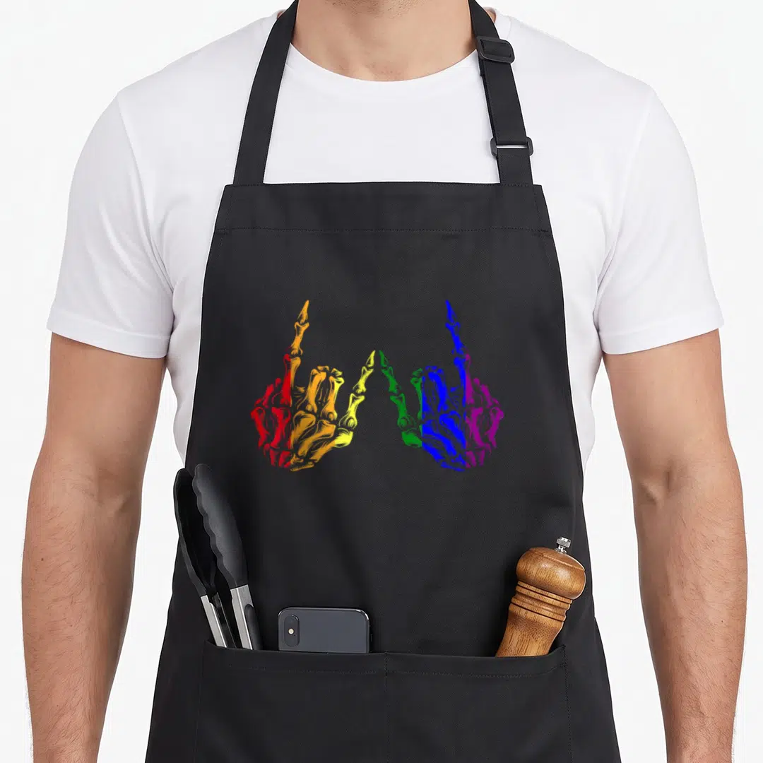 Rainbow skeleton apron - Two mirrored skeletal hands colored in red, orange, yellow, green, blue, and purple stripes — shown on a black cotton canvas apron against a white background