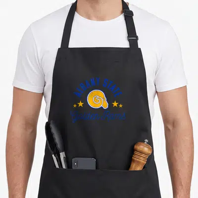 State university golden apron - Albany State ram head logo with arched text and yellow stars in distressed blue and gold — shown on a black cotton canvas apron against a white background