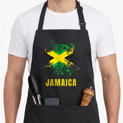 Jamaica jamaican apron - Distressed Jamaican flag with paint splatter and yellow JAMAICA text — shown on a black cotton canvas apron against a white background