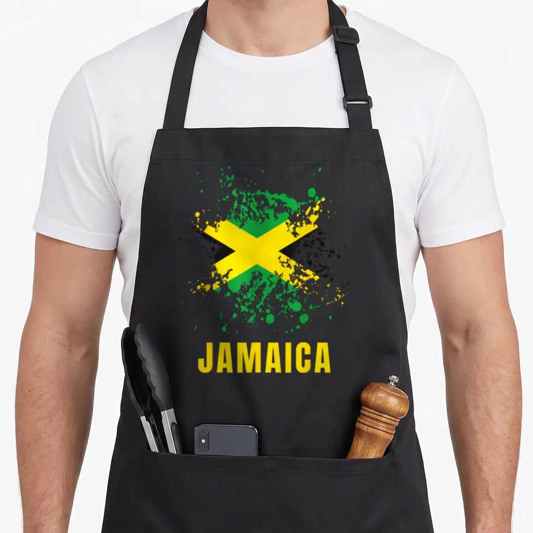 Jamaica jamaican apron - Distressed Jamaican flag with paint splatter and yellow JAMAICA text — shown on a black cotton canvas apron against a white background