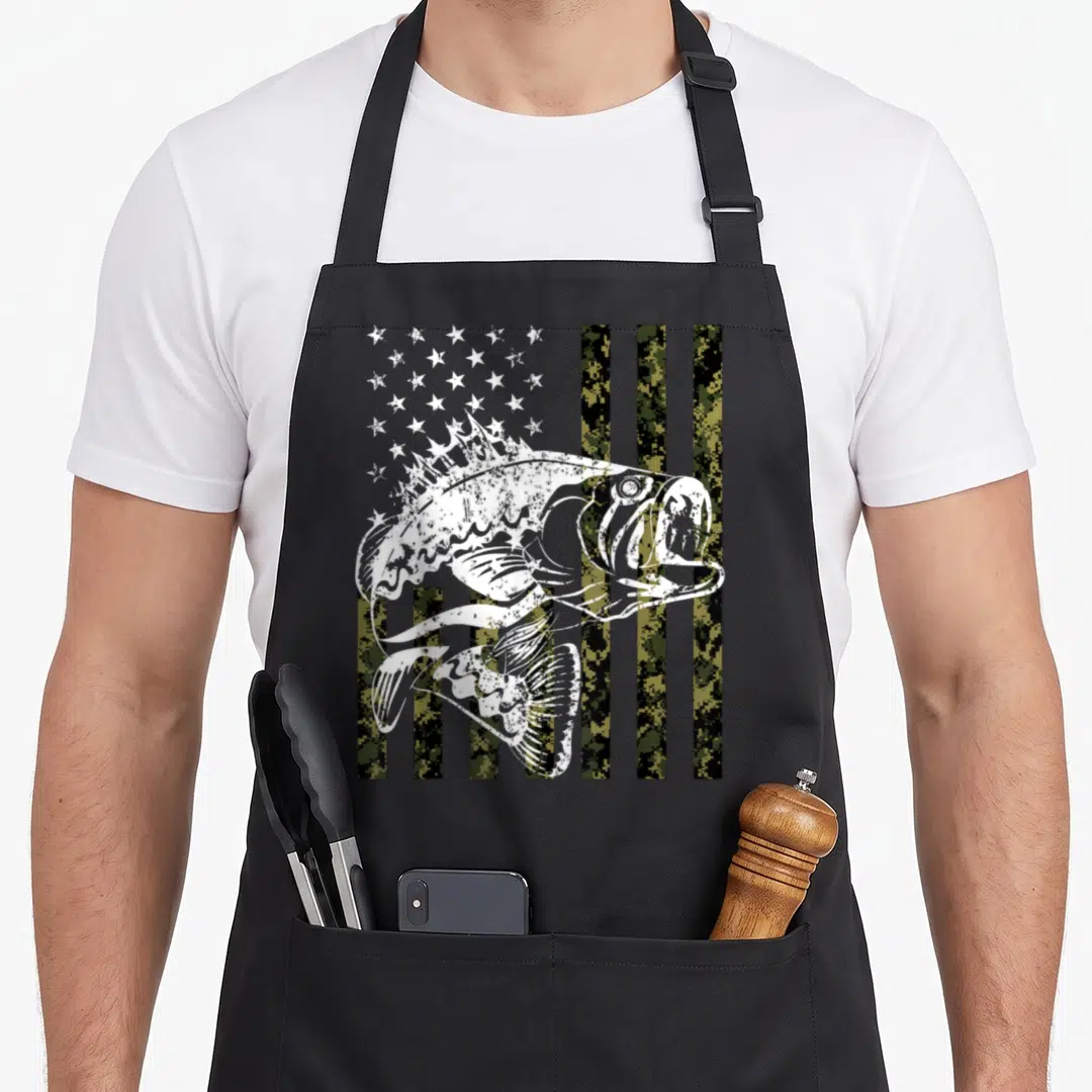 Flag patriotic aprons - Distressed white bass fish over green brown black camo US flag pattern — shown on a black cotton canvas apron against a white background