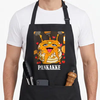 Pun funny naughty aprons - Cartoon pancake stack with face, syrup, strawberries, hearts, and PANKAKKE text — shown on a black cotton canvas apron against a white background
