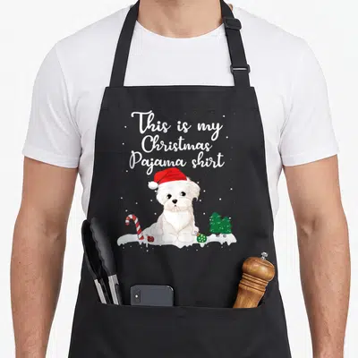 Pajama christmas dog apron - Cartoon white dog in red hat with This is my Christmas Pajama shirt text and candy cane — shown on a black cotton canvas apron against a white background