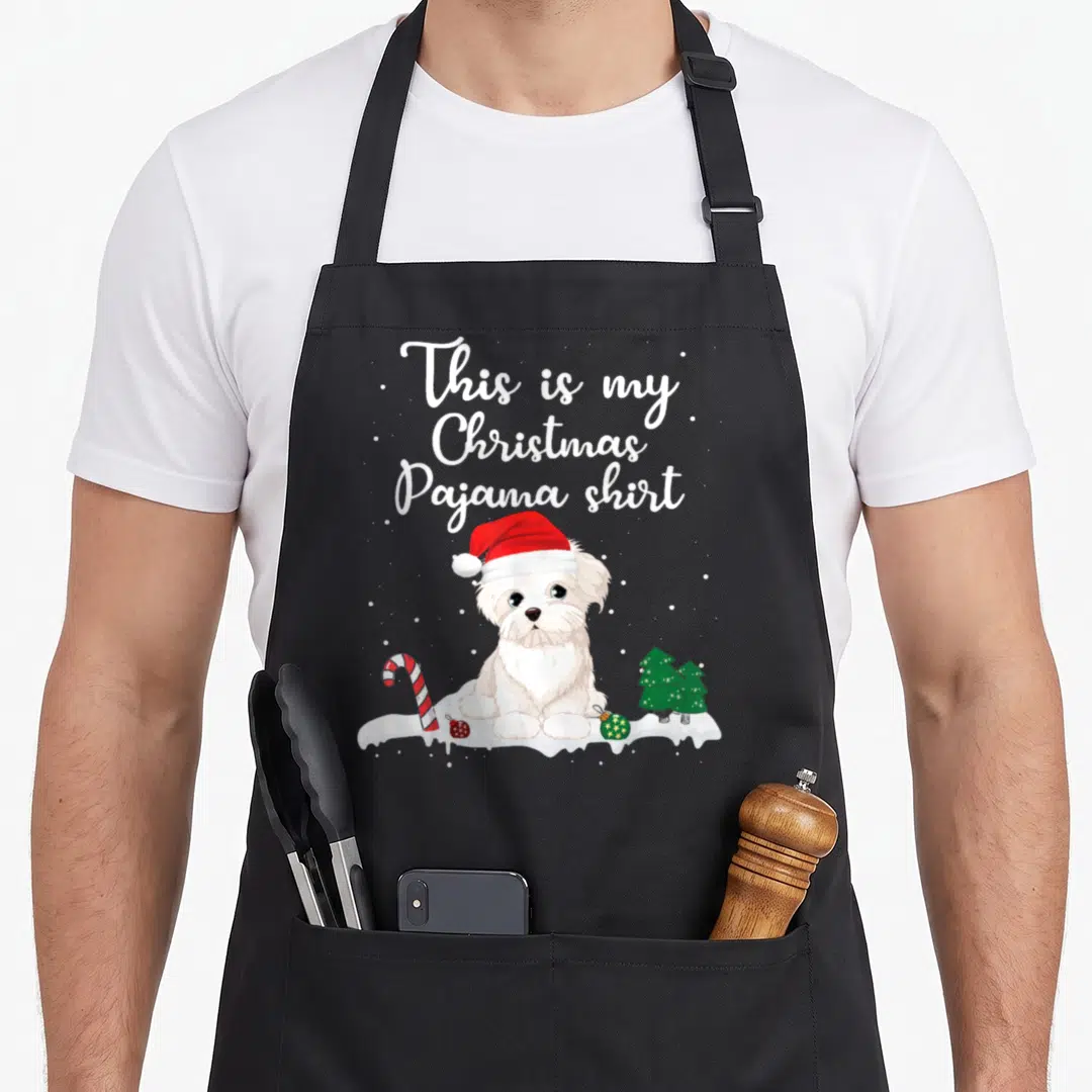 Pajama christmas dog apron - Cartoon white dog in red hat with This is my Christmas Pajama shirt text and candy cane — shown on a black cotton canvas apron against a white background