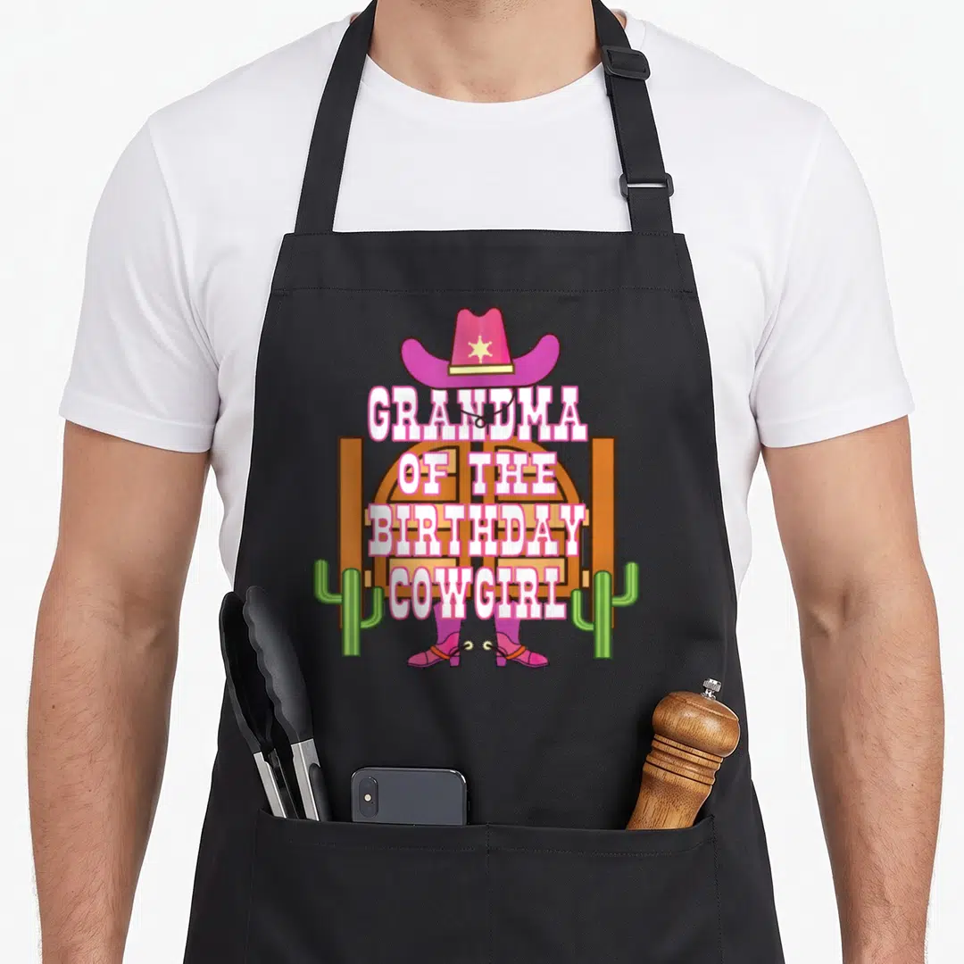 Grandma cowgirl aprons - Pink cowboy hat, stable door, boots with spurs, and GRANDMA OF THE BIRTHDAY COWGIRL text — shown on a black cotton canvas apron against a white background