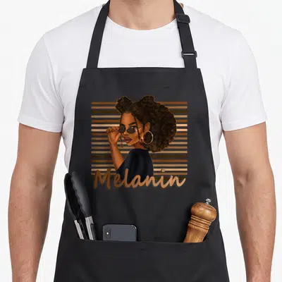 Magic hair apron - Cartoon woman with afro and sunglasses over brown stripes with Melanin text — shown on a black cotton canvas apron against a white background