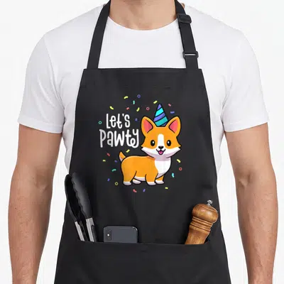 Pawty corgi apron - Cartoon corgi wearing striped hat next to Let's Pawty text with confetti — shown on a black cotton canvas apron against a white background