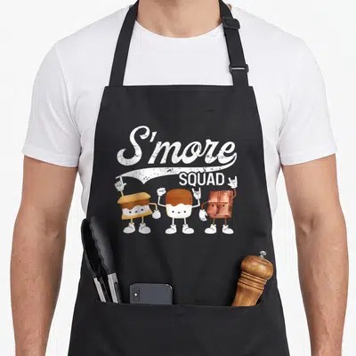 Smore squad camping apron - Three cartoon s'more ingredients with white gloves under S'more SQUAD script text — shown on a black cotton canvas apron against a white background