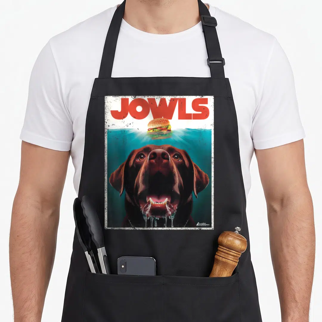 Jowl labrador apron - Brown dog swimming underwater below red JOWLS text and floating hamburger — shown on a black cotton canvas apron against a white background