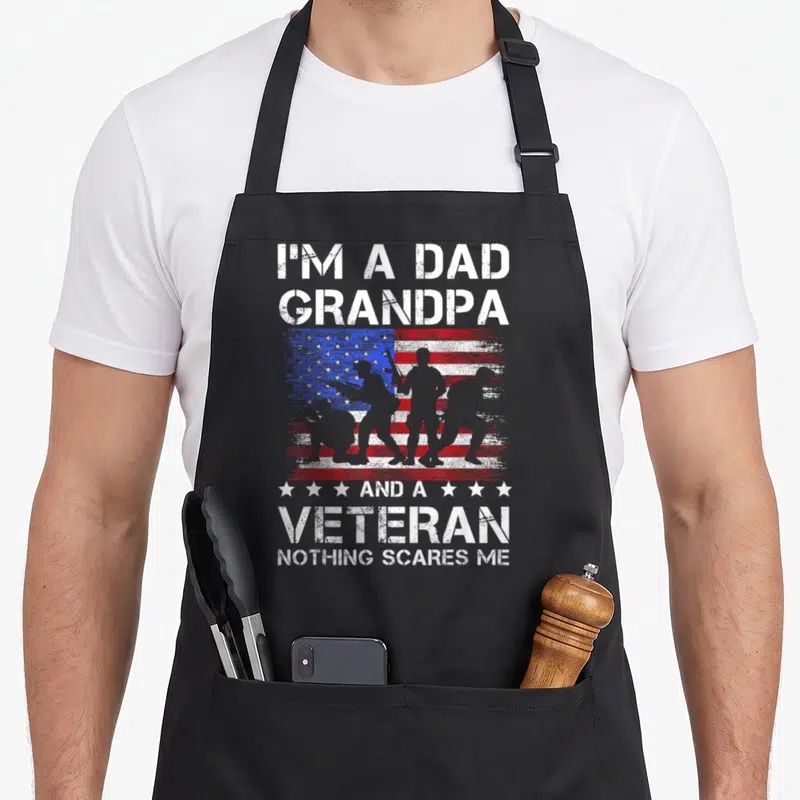 Veteran scare father day apron - I'M A DAD GRANDPA VETERAN text over four soldier silhouettes on distressed flag — shown on a black cotton canvas apron against a white background