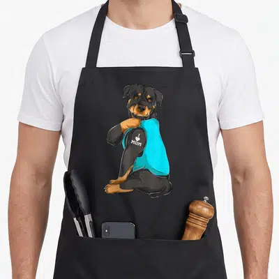 Tattoo dog apron - Cartoon rottweiler lifting cyan sleeve to show white I Love Mom tattoo on arm — shown on a black cotton canvas apron against a white background