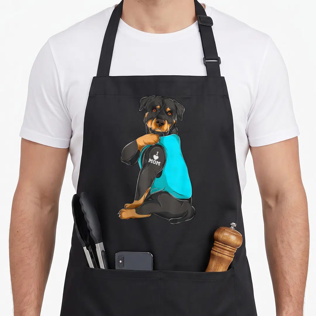 Tattoo dog apron - Cartoon rottweiler lifting cyan sleeve to show white I Love Mom tattoo on arm — shown on a black cotton canvas apron against a white background