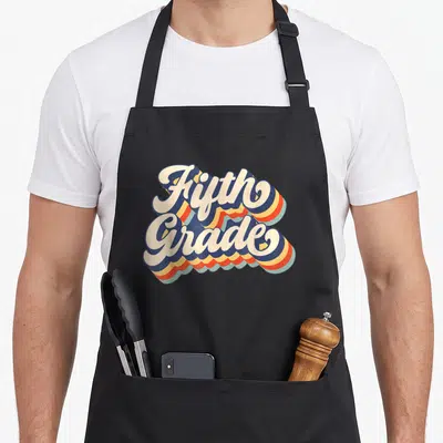 Sunset teacher apron - Retro stacked Fifth Grade typography with cream script and multi-colored shadows — shown on a black cotton canvas apron against a white background