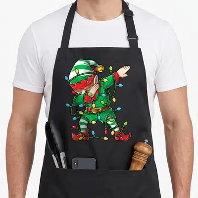 Elf christmas tree apron - Cartoon elf dabbing while tangled in multicolored Christmas lights — shown on a black cotton canvas apron against a white background