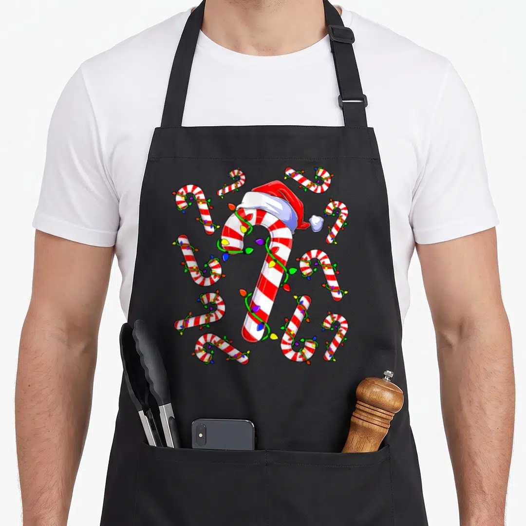 Christmas candy cane apron - Cartoon candy canes with santa hat and multi-colored lights on red and white stripes — shown on a black cotton canvas apron against a white background