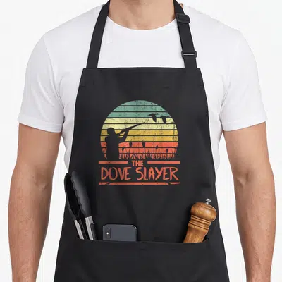 Hunt funny dove hunting apron - Retro hunter silhouette with shotgun against striped sun and flying birds above — shown on a black cotton canvas apron against a white background