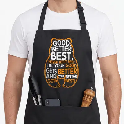 Rest bear apron - Orange and white Good Better Best text forming a bear outline shape — shown on a black cotton canvas apron against a white background