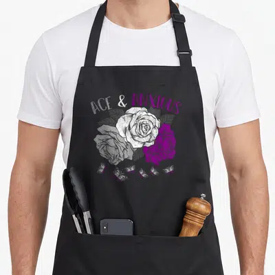Asexual pride apron - ACE & ANXIOUS text above three roses and six butterflies in purple, white, and grey — shown on a black cotton canvas apron against a white background