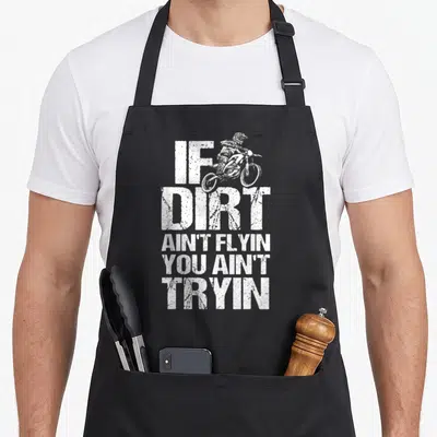 Bike motorcycle aprons - White distressed text If Dirt Ain't Flyin You Ain't Tryin with jumping motocross rider — shown on a black cotton canvas apron against a white background